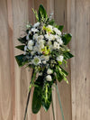 Standing spray with white roses, green cymbidium orchids, and tropical foliage on easel