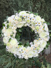 White funeral wreath with roses, chrysanthemums, lilies, and daisies on a green easel